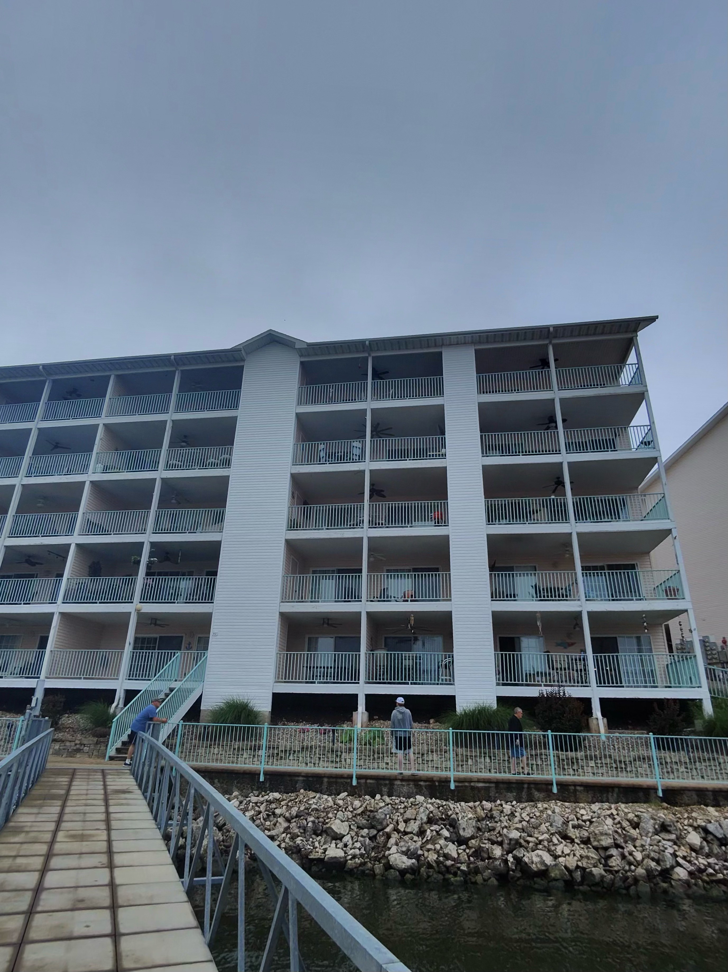 White multi-story condominium exterior with balconies viewed from a dock walkway.