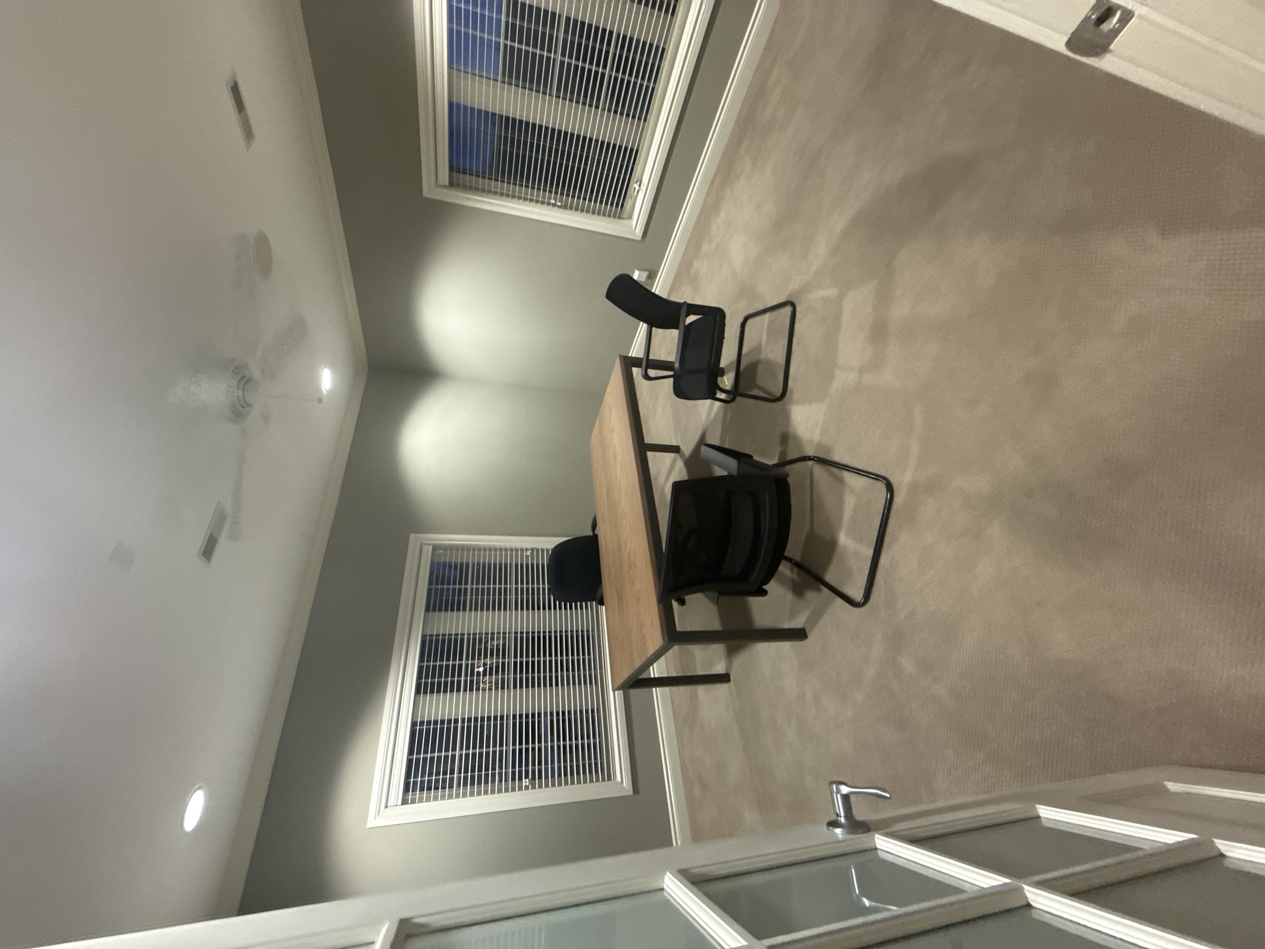Gray-walled commercial office with a wood table, black chairs, recessed lights, windows with blinds, and carpet.