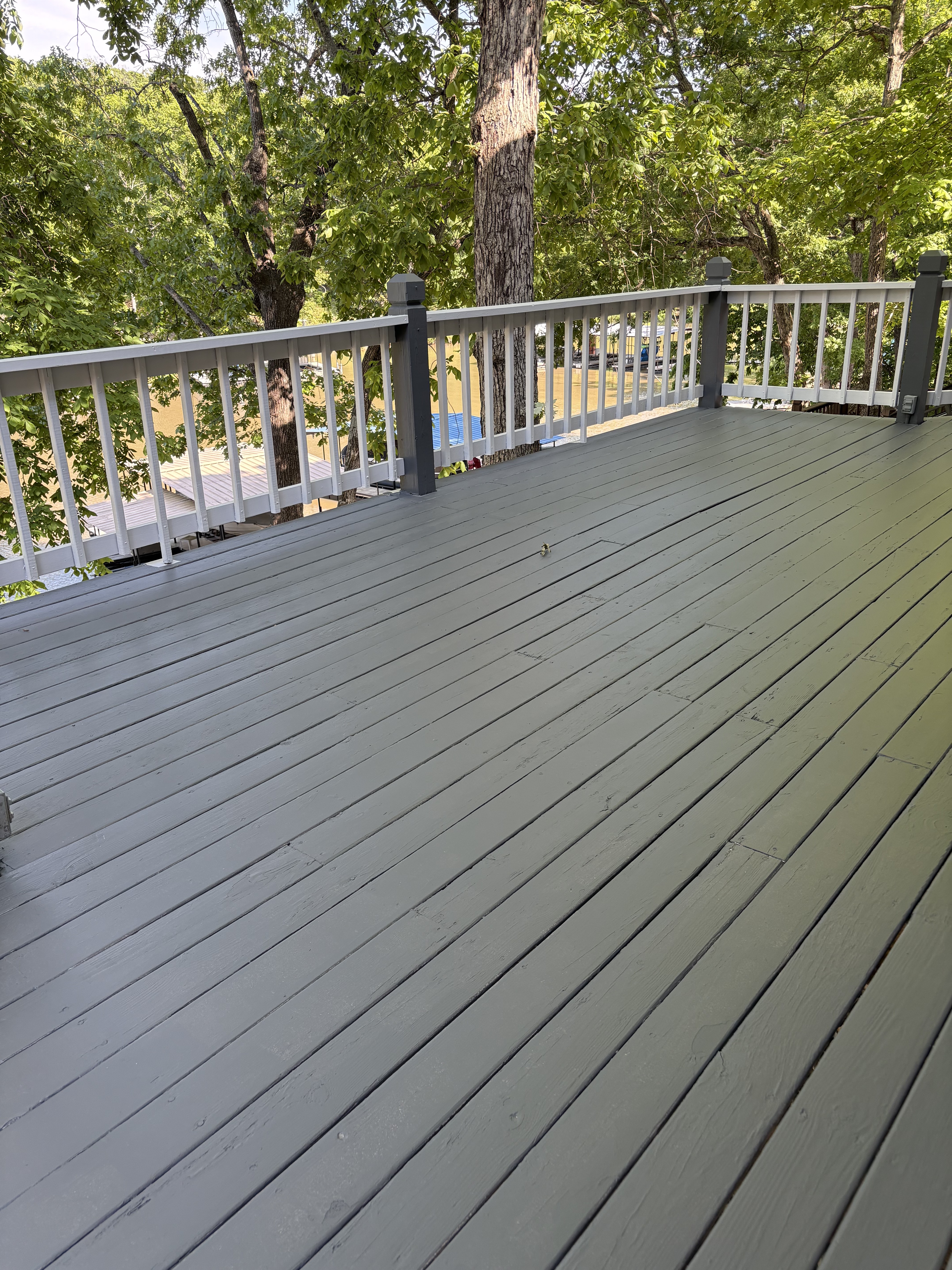 Gray-painted wood deck with white and dark-gray railing beside mature trees.